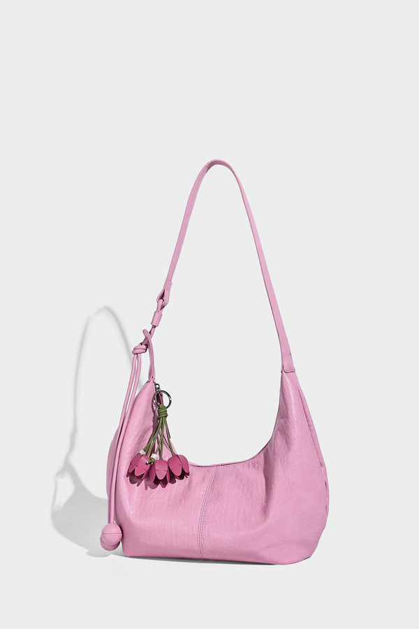 Slouchy crescent half-moon shoulder bag in pink pebbled textured finish with floral charm and knotted side detail, detail