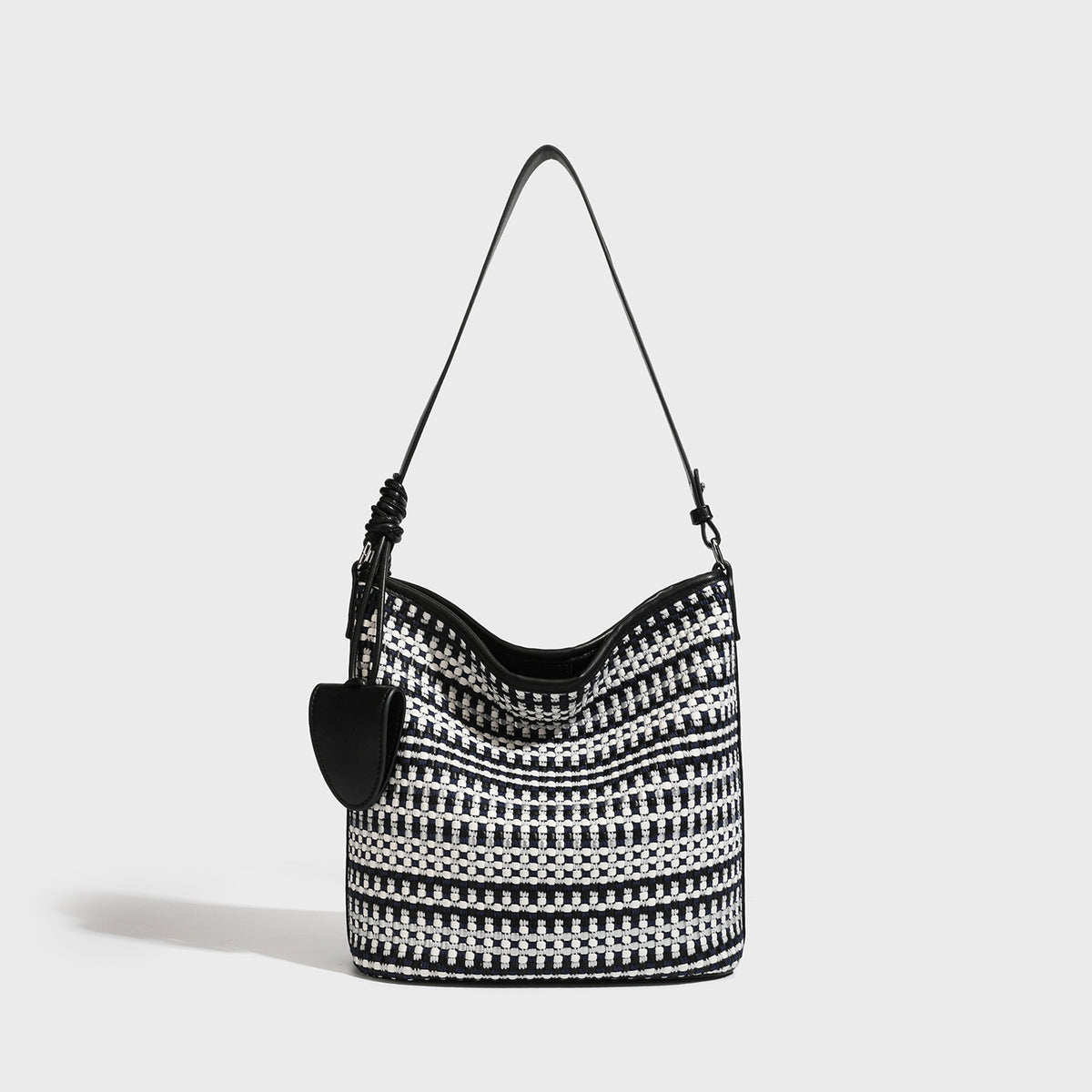 Woven stripe bucket shoulder bag in cream and dark brown with leather-look trim, knotted adjustable strap, and small shield