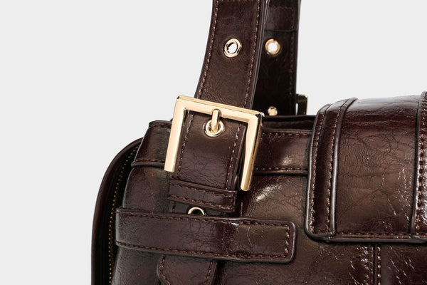 Structured leather-look satchel bag with heart padlock charm, star charm, gold-tone buckle hardware, dual top handles, and