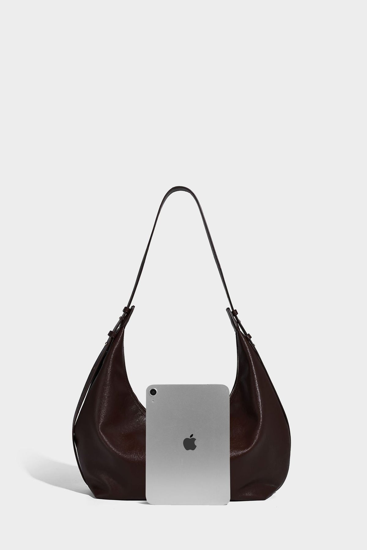 Lässig fallende, sichelförmige Hobo-Schultertasche in glatter dunkelbrauner Lederoptik mit Logo-Anhänger in Goldoptik und verstellbarem Schulterriemen