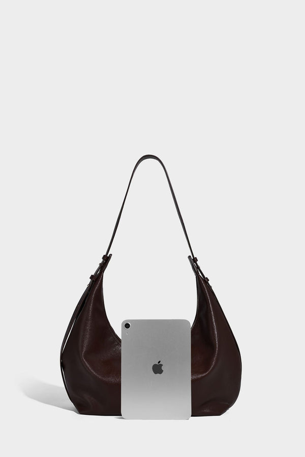 Lässig fallende, sichelförmige Hobo-Schultertasche in glatter dunkelbrauner Lederoptik mit Logo-Anhänger in Goldoptik und verstellbarem Schulterriemen