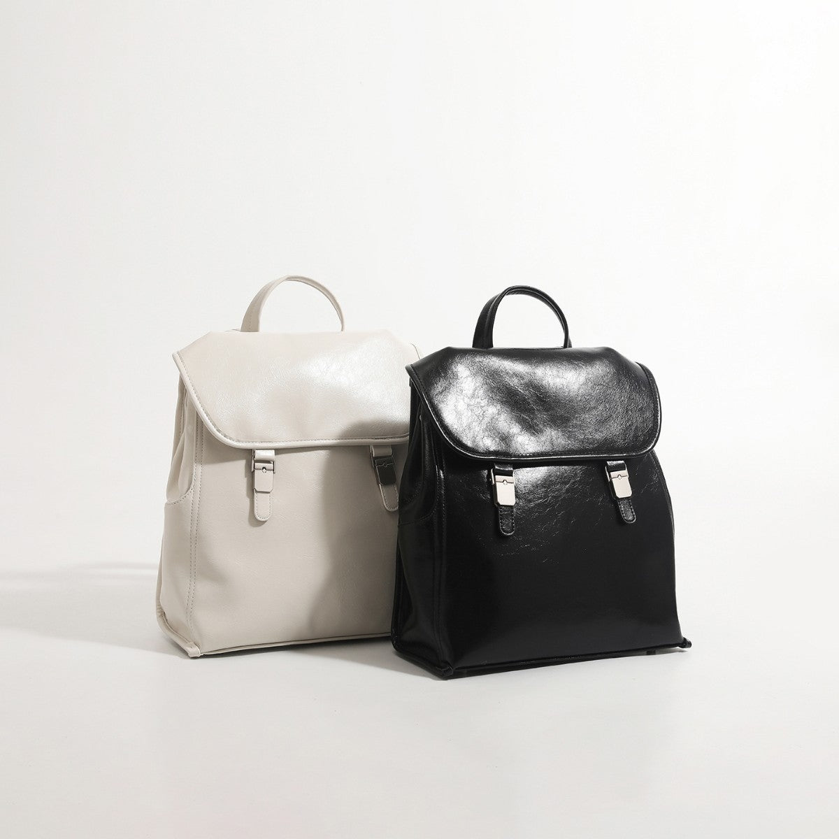 Structured glossy leather-look flap backpack handbag with dual buckle closures, top handle, and silver-tone hardware, detail