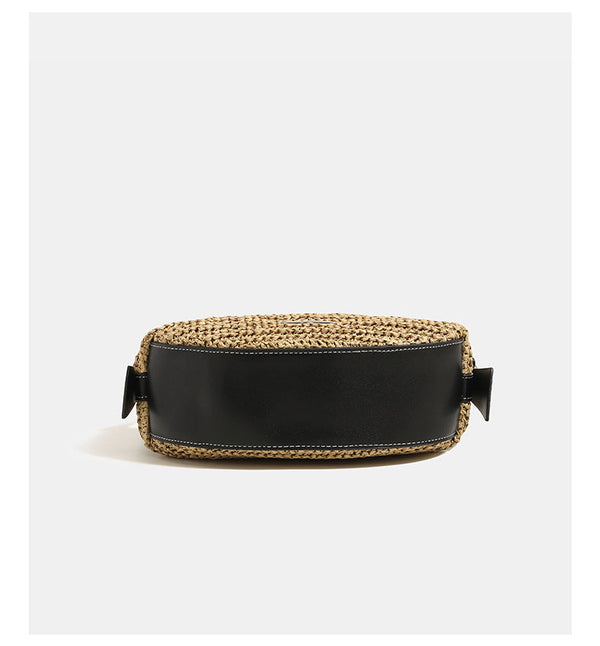 Compact crescent-shaped woven straw crossbody bag with black leather-look trim, top zip closure, and adjustable shoulder