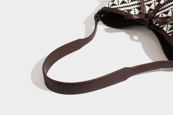 Woven geometric bucket shoulder bag in white and dark brown two-tone pattern with leather-look trim and drawstring top