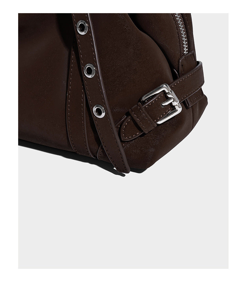 Weiche, zylinderförmige Schultertasche in Dunkelbraun mit silberfarbenen Riemen mit Ösen, Reißverschluss oben, seitlichen Schnallenbeschlägen und Quaste