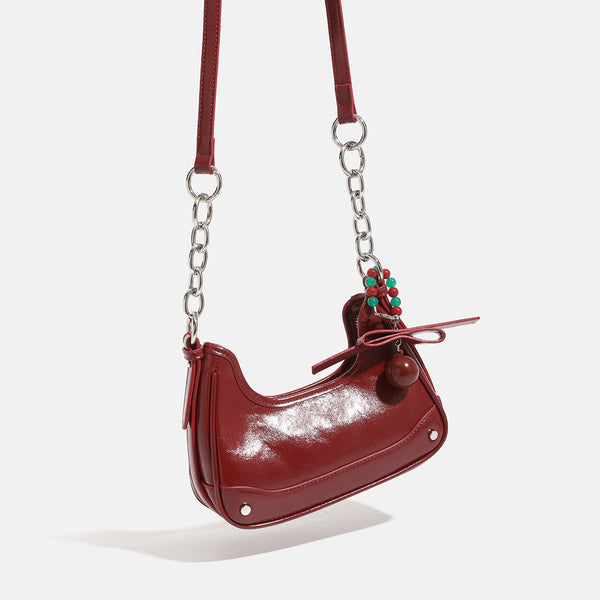 Small glossy cherry red crescent shoulder bag with silver chain strap, bead and tassel charm, and round pendant, detail view