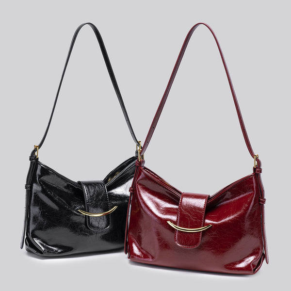 Glossy burgundy leather-look shoulder bag with curved gold-tone bar front closure, crinkled oil-wax texture, and adjustable