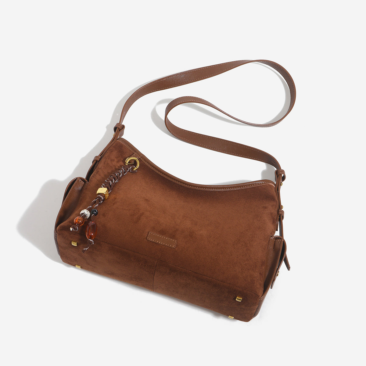 Caramel brown slouchy hobo shoulder bag with matte suede-like finish, braided tassel charm, brass-tone hardware, and, detail