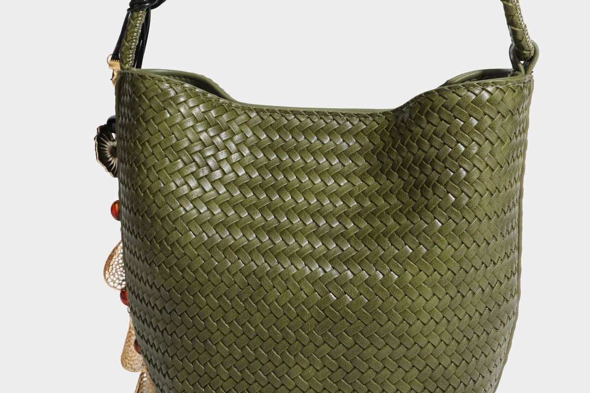 Olive green woven leather-look bucket bag with braided crossbody strap, knotted adjustment, and gold-tone tassel charm with