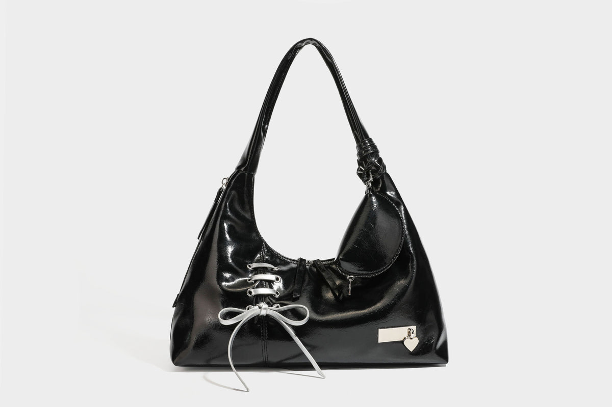Weich fallende Hobo-Schultertasche in glänzender Lederoptik mit silberfarbenen Ösen zum Schnüren und Schleifenband auf der Vorderseite, Detailansicht