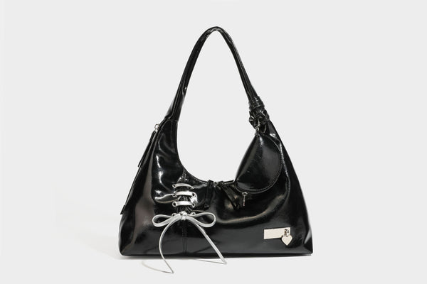 Weich fallende Hobo-Schultertasche in glänzender Lederoptik mit silberfarbenen Ösen zum Schnüren und Schleifenband auf der Vorderseite, Detailansicht