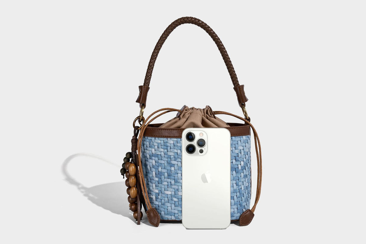 Small light blue woven bucket bag with brown leather-look trim, braided top handle, brass-tone ring hardware, drawstring