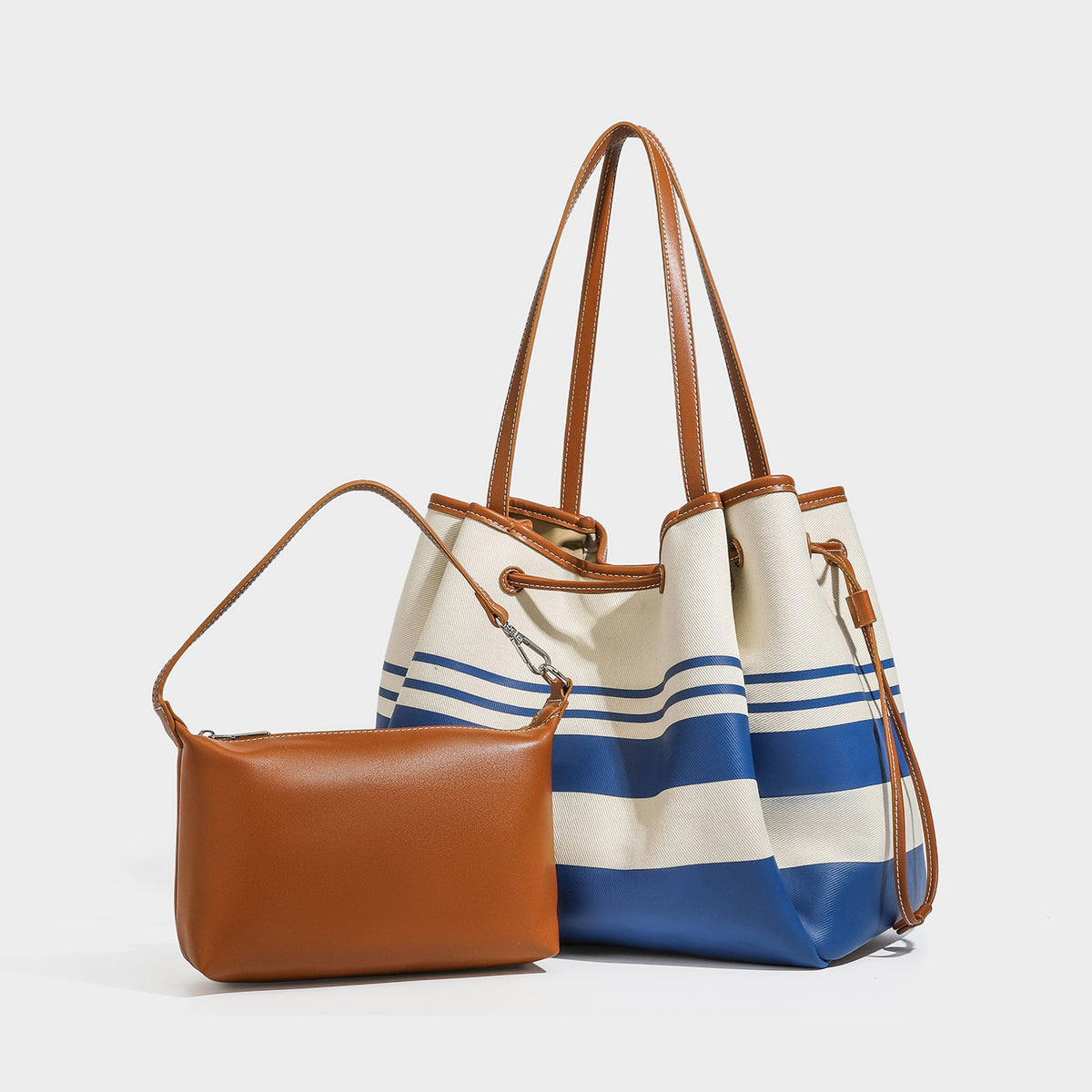 Large cream and navy striped canvas bucket tote bag with tan leather-look trim, drawstring closure, and double shoulder