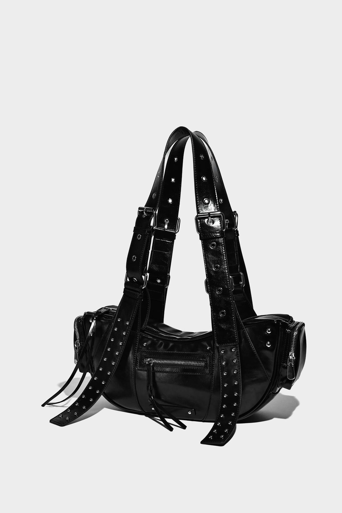 Glossy black crescent shoulder bag with silver-tone rivets, multiple zip pockets, and long adjustable studded straps, detail
