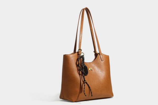 Structured smooth leather-look tote bag with long shoulder strap, gold-tone hardware, and hanging tassel-coin charm, detail