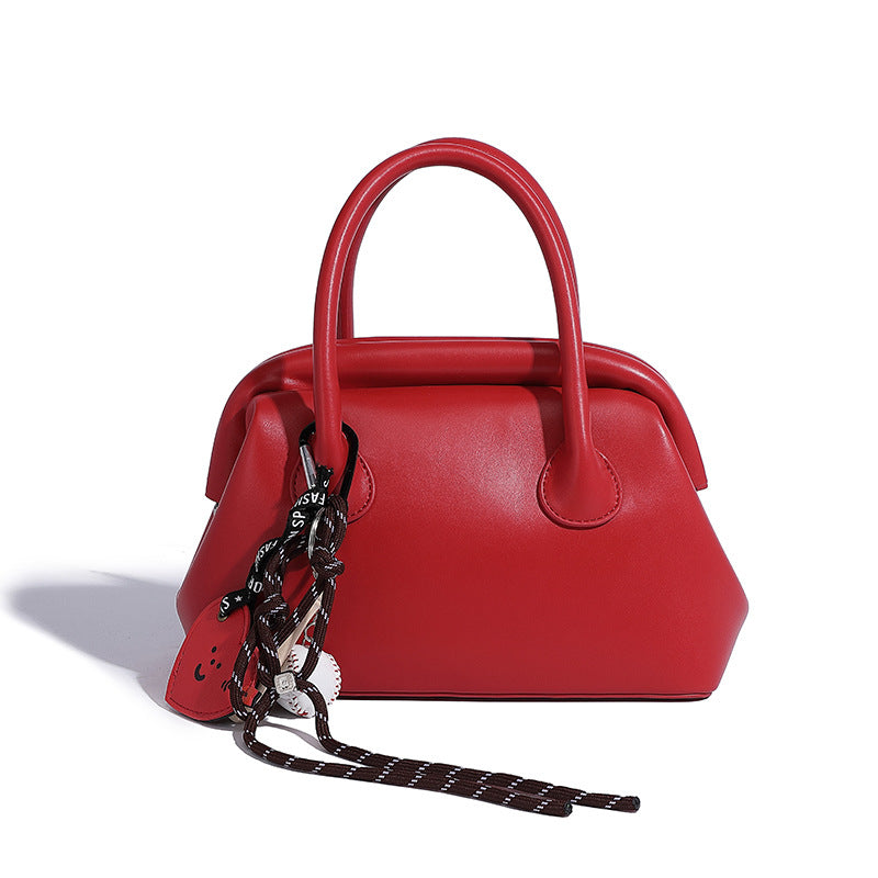 Small structured shell top-handle bag in red with heart charm and braided cord detail, smooth leather-look finish, detail