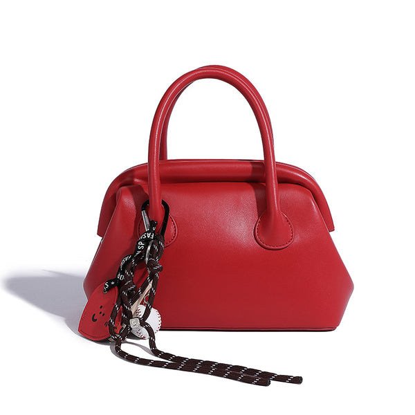 Small structured shell top-handle bag in red with heart charm and braided cord detail, smooth leather-look finish, detail