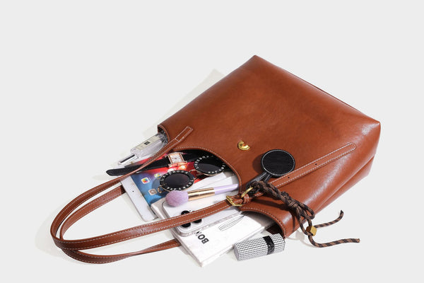 Structured smooth leather-look tote bag with long shoulder strap, gold-tone hardware, and hanging tassel-coin charm, detail