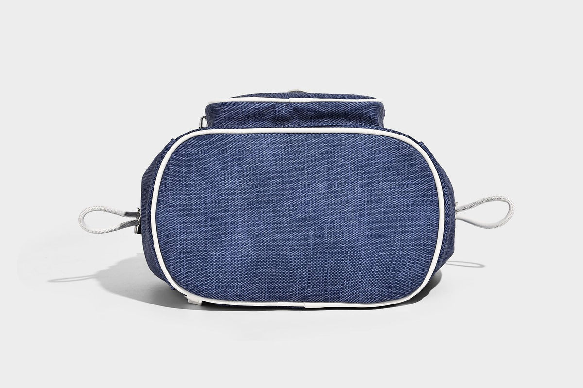 Compact denim drawstring backpack with white leather-look piping, flap-top buckle closure, front zip pocket, and silver-tone