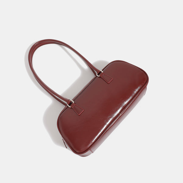 Rounded baguette shoulder bag with glossy leather-look finish, double-pull zip top, dual top handles, and silver-tone, detail