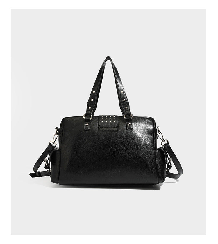 Structured pink leather-look satchel bag with gunmetal studded trim, rectangular buckle strap, dual top handles, and, detail