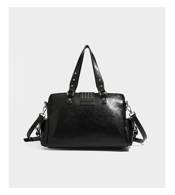Structured pink leather-look satchel bag with gunmetal studded trim, rectangular buckle strap, dual top handles, and, detail