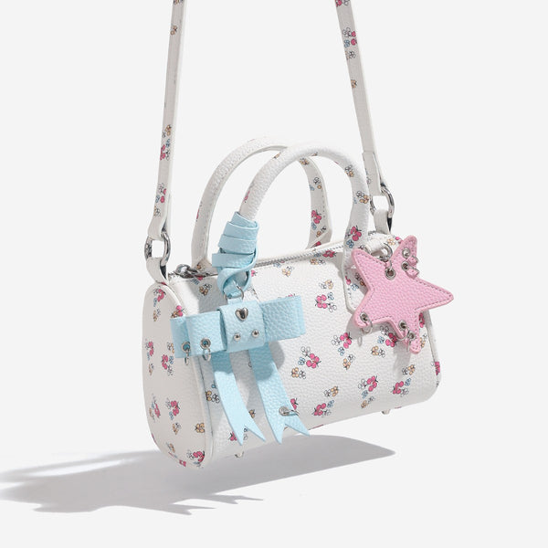 Weiße Mini-Boston-Handtasche mit genarbter Oberfläche und Blumen- oder Kirschprint, pastellblauem Schleifenanhänger, rosafarbenem Sternanhänger und zwei oberen Henkeln