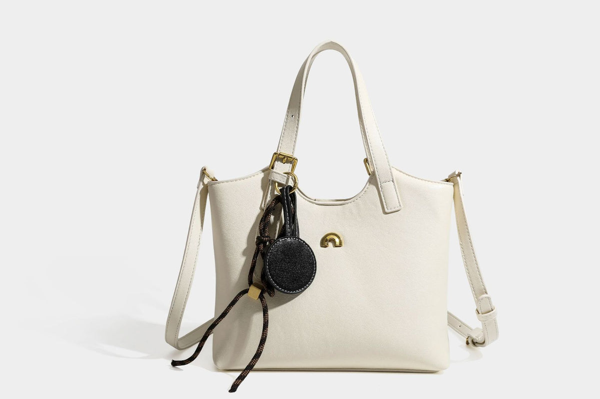 Structured smooth leather-look tote bag with long shoulder strap, gold-tone hardware, and hanging tassel-coin charm, detail