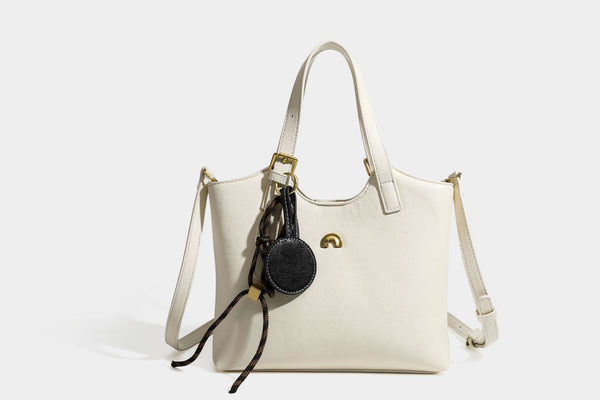 Structured smooth leather-look tote bag with long shoulder strap, gold-tone hardware, and hanging tassel-coin charm, detail