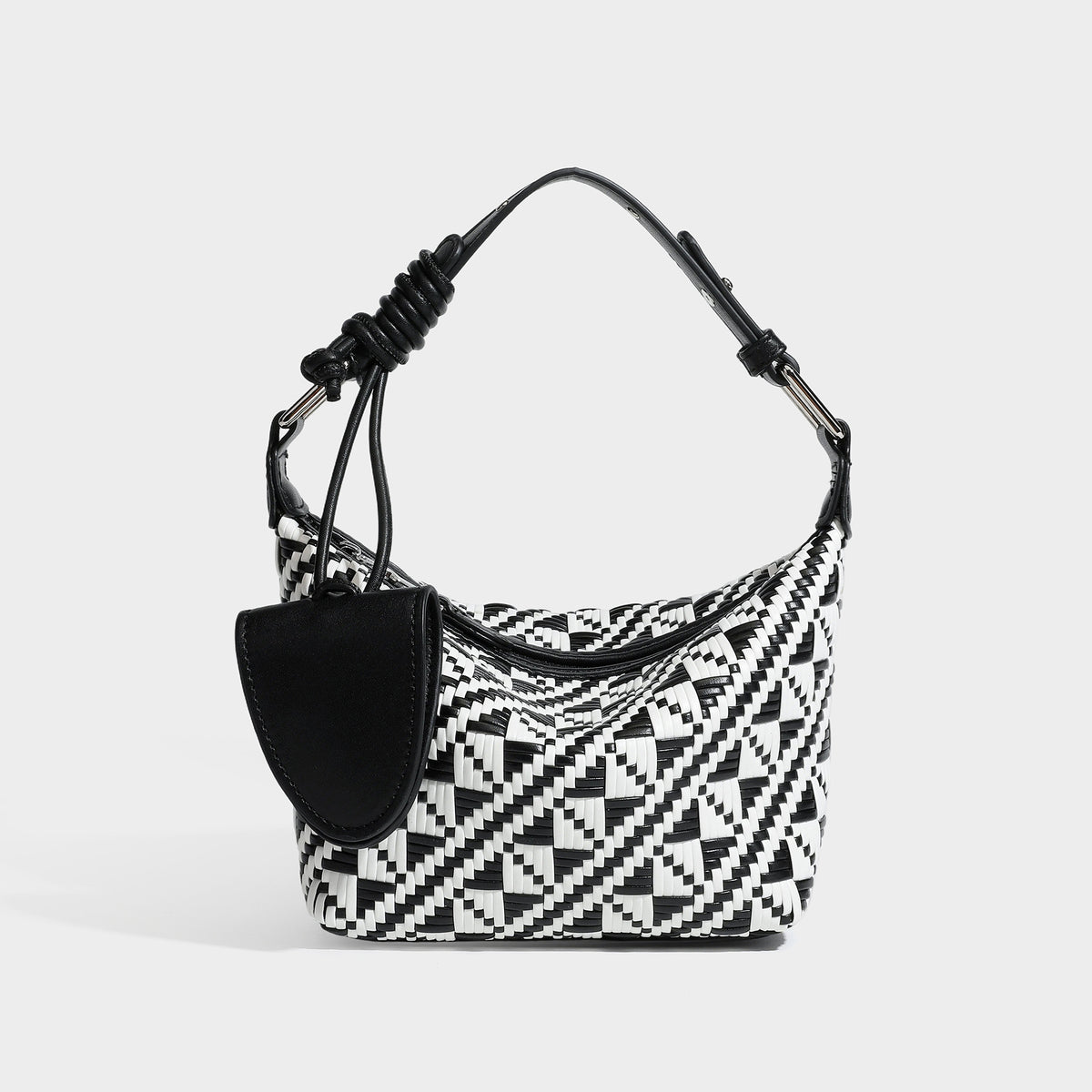 Kleine gewebte Schultertasche mit geometrischem Schwarz-Weiß-Muster, glatten dunkelbraunen Details in Lederoptik, geknotetem verstellbarem Riemen, Seitenansicht