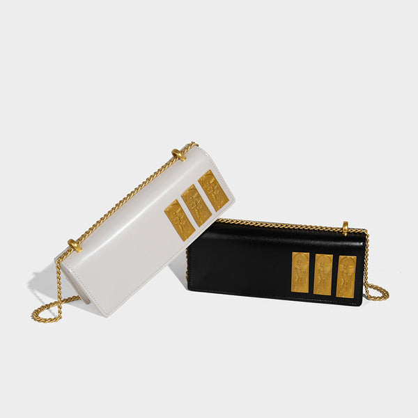 Structured rectangular crossbody bag with glossy finish, three vertical gold-tone embossed plaques, and gold chain strap