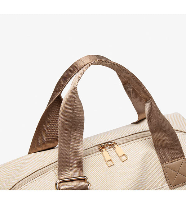 Structured woven duffel bag with dual tan webbing handles, detachable shoulder strap, top zip closure, and gold-tone