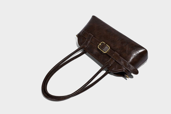 Strukturierte dunkelbraune Henkeltasche mit Öl-Wachs-Finish, vorderer Gürtelschnalle, goldfarbenen Beschlägen und zwei Tragegriffen, Detailansicht