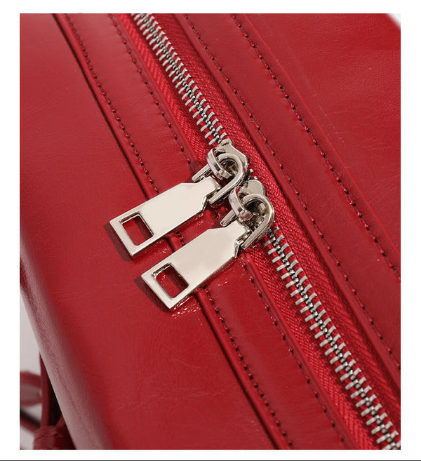 Strukturierte, glänzende trapezförmige Schultertasche mit zwei Tragegriffen, umlaufendem Riemen, silberfarbener Schnalle und hängendem