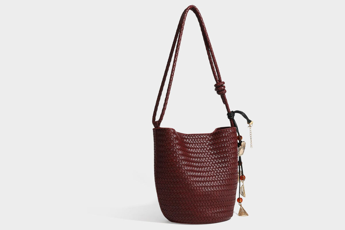 Olive green woven leather-look bucket bag with braided crossbody strap, knotted adjustment, and gold-tone tassel charm with