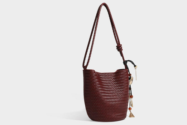 Olive green woven leather-look bucket bag with braided crossbody strap, knotted adjustment, and gold-tone tassel charm with