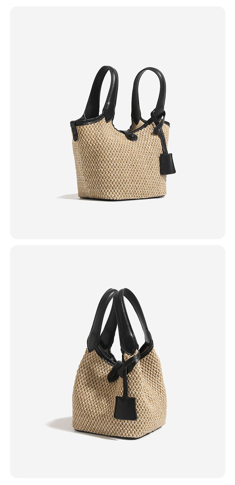 Woven beige straw bucket bag with black leather-look trim, dual top handles, detachable shoulder strap, and front snap