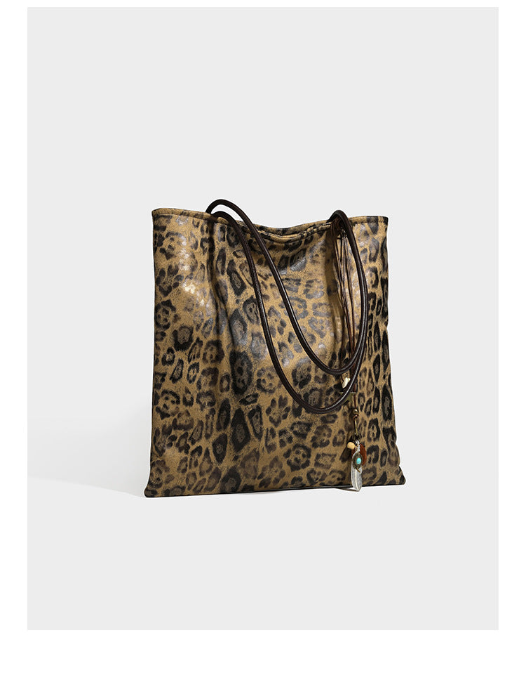 Large leopard print shoulder tote bag in tan and brown with slim dark straps and dangling beaded charm hardware, detail view
