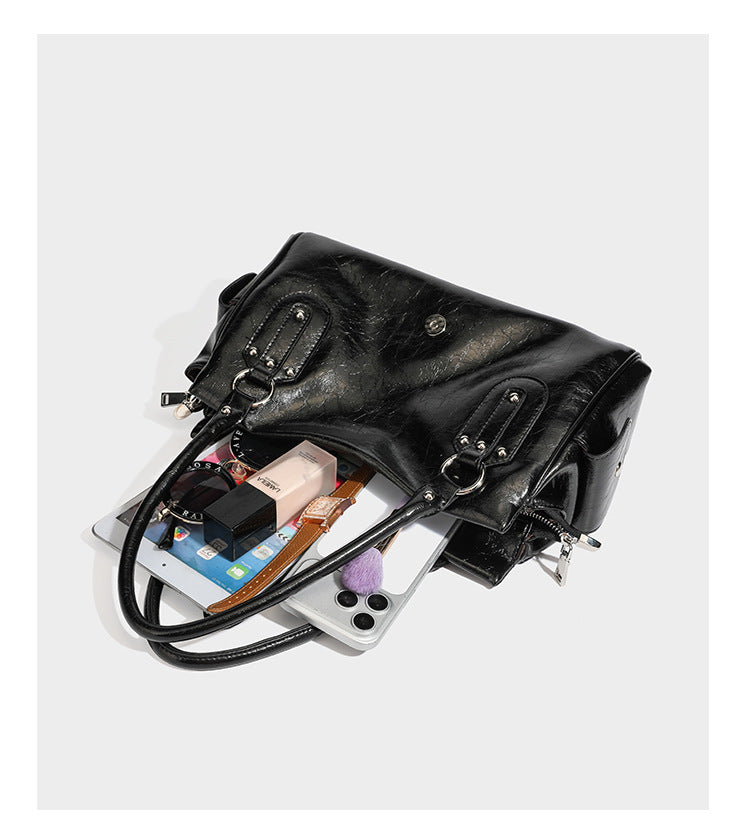 Glänzende, geknautschte Barrel-Satchel mit zwei oberen Tragegriffen, vorderem Klappen-Riemen-Panel, Ring- und Nietenbeschlägen sowie einem abnehmbaren