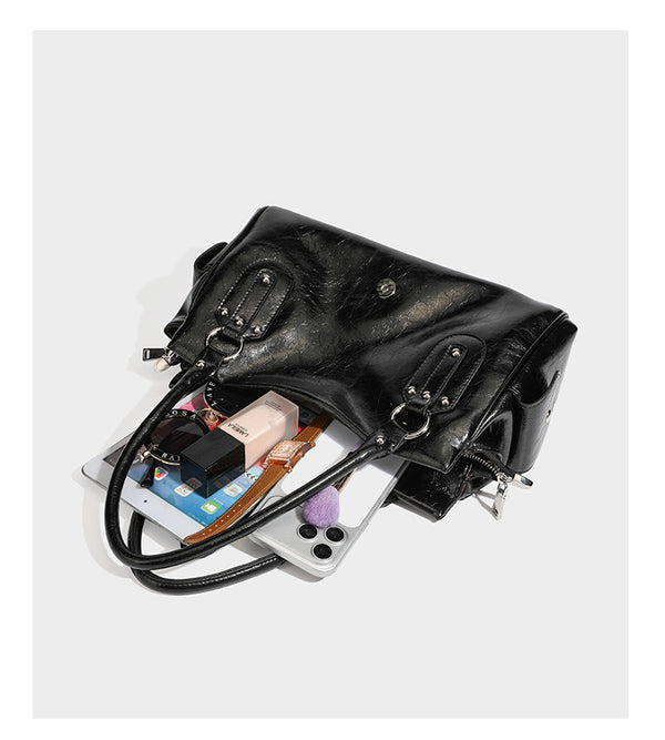 Glänzende, geknautschte Barrel-Satchel mit zwei oberen Tragegriffen, vorderem Klappen-Riemen-Panel, Ring- und Nietenbeschlägen sowie einem abnehmbaren
