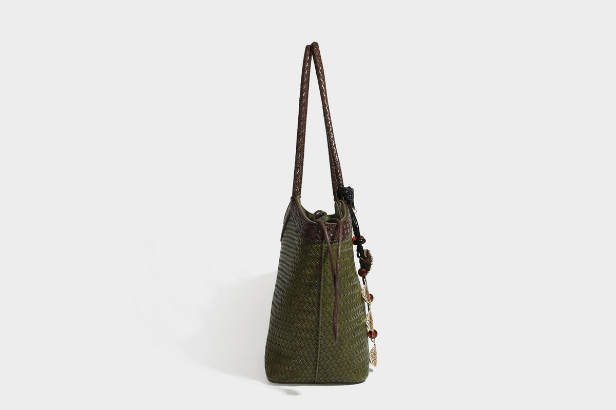 Olivgrüne Tote-Bag in Korbgeflecht-Optik mit dunkelbraunen geflochtenen Schulterriemen, seitlichen Kordelzügen und Perlenanhänger in Goldoptik