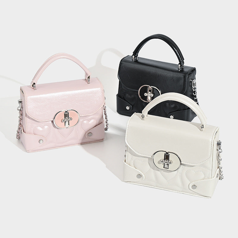 Small structured heart-quilted PU top-handle box bag with silver-tone chain crossbody strap and oval turn-lock clasp, detail