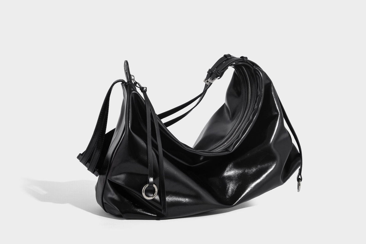 Glossy black slouchy hobo shoulder bag with zip closure, silver-tone ring hardware, and adjustable crossbody strap, detail