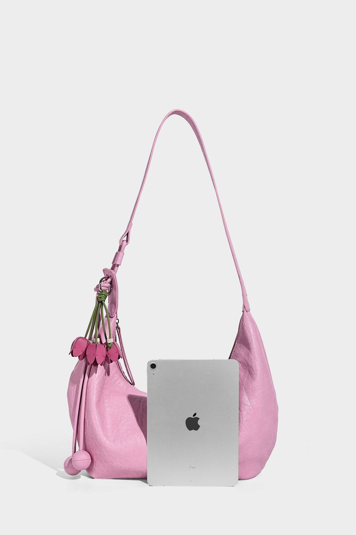 Slouchy crescent half-moon shoulder bag in pink pebbled textured finish with floral charm and knotted side detail, detail