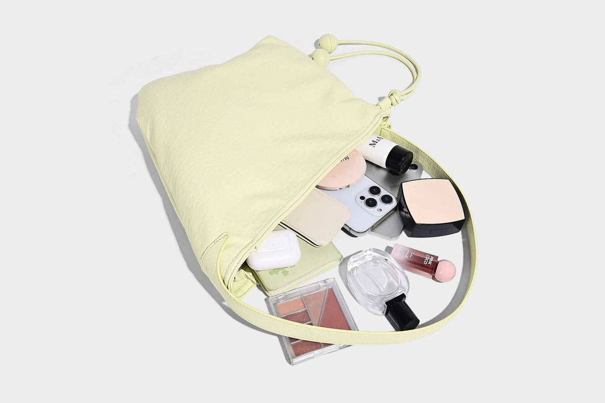 Slouchy hobo shoulder bag in pale yellow with slim strap, drawstring bead closure, and pink tulip floral charm, detail view