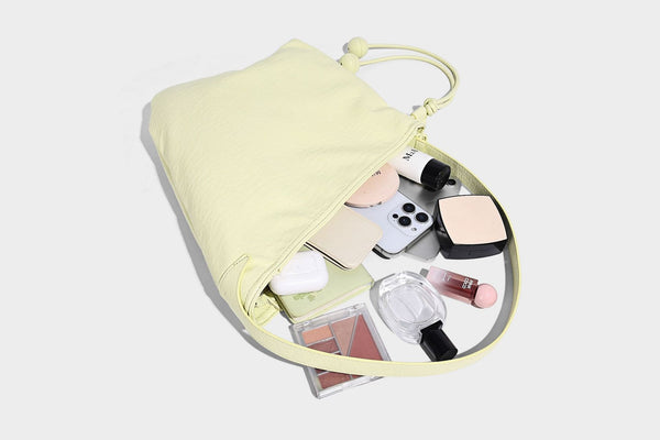 Slouchy hobo shoulder bag in pale yellow with slim strap, drawstring bead closure, and pink tulip floral charm, detail view