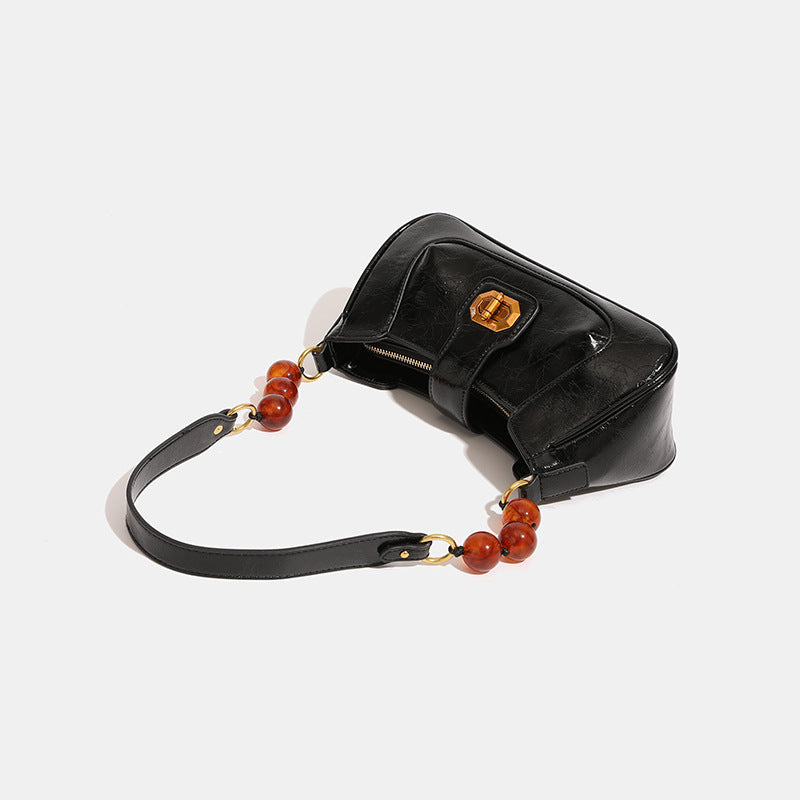 Structured glossy crinkled-finish shoulder bag with amber resin bead strap accent and gold-tone turn-lock closure, detail