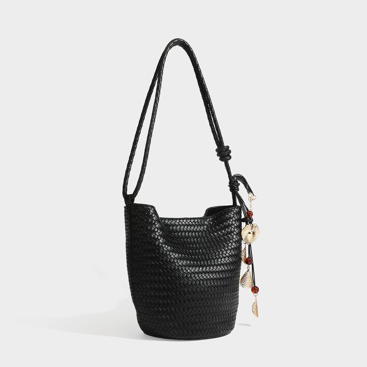 Olive green woven leather-look bucket bag with braided crossbody strap, knotted adjustment, and gold-tone tassel charm with