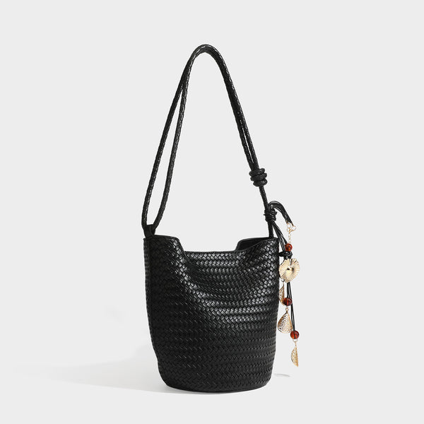 Olive green woven leather-look bucket bag with braided crossbody strap, knotted adjustment, and gold-tone tassel charm with