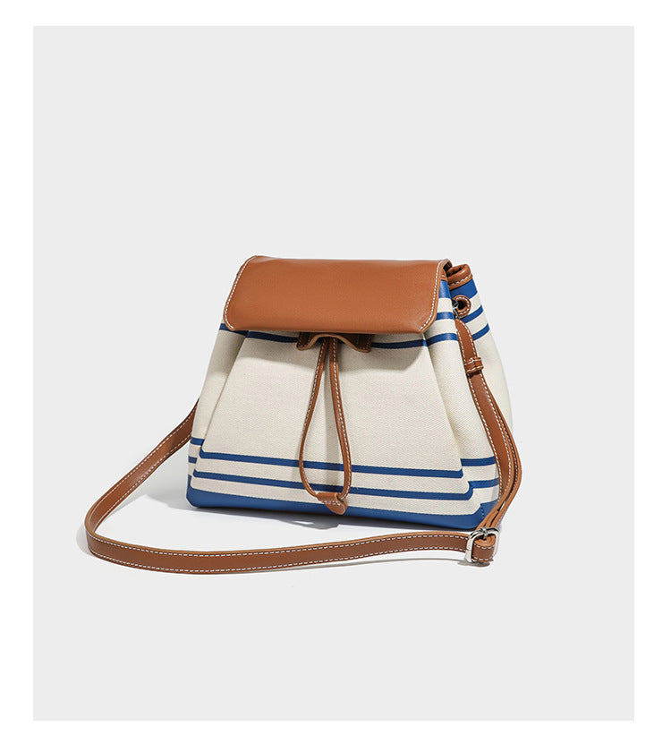 Cream canvas bucket bag with blue horizontal stripes, tan leather-look flap and trim, drawstring closure, silver-tone, detail